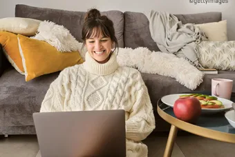 Vrouw in woonkamer voor de zetel op de grond typend op laptop